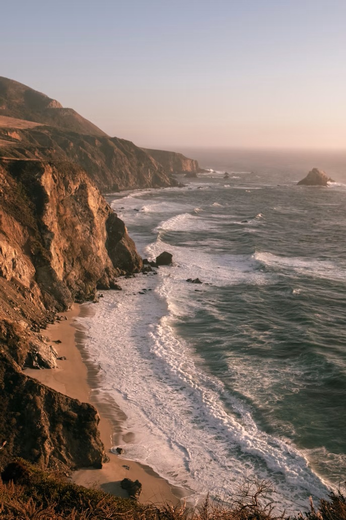 Aerial view of the rugged Big Sur coastline with mist hitting the dark cliffs