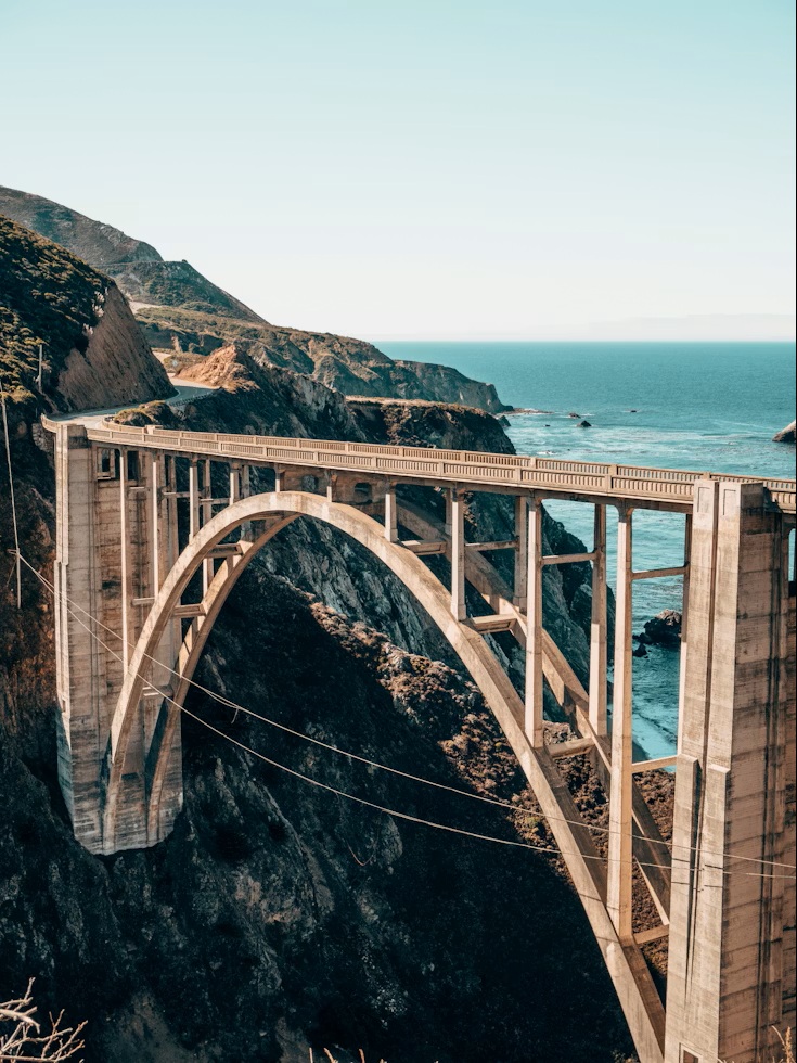 Close-up of Bixby Creek Bridge's concrete arch with the Pacific Ocean waves crashing below