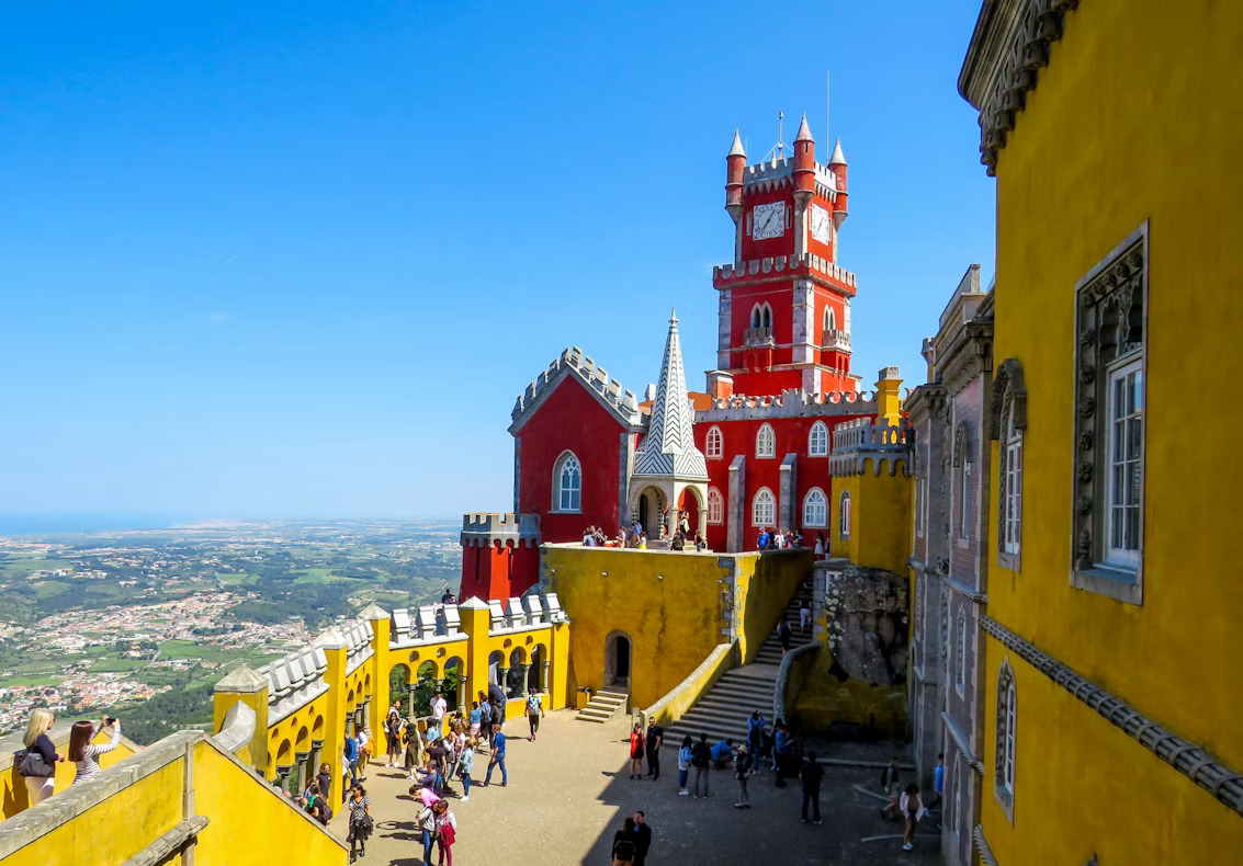 The bright yellow and red facades of Pena Palace against a blue sky in Sintra.