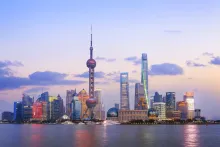 A panoramic view of Shanghai's futuristic Pudong skyline at dusk, featuring the Oriental Pearl TV Tower and Shanghai Tower, with their lights reflecting on the Huangpu River.