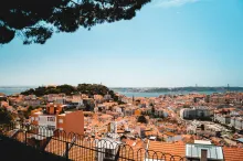 Panoramic view of Lisbon with colorful rooftops, the Tagus River, and historic hills under a clear sky, showcasing the city’s vibrant charm and iconic architecture.