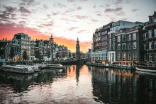 Panoramic view of Amsterdam canals with historic Dutch townhouses, bridges, bicycles, and waterfront architecture under warm evening light in the Netherlands.