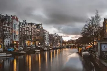 Panoramic view of Amsterdam with canal houses, bridges, bicycles, and historic Dutch architecture reflecting on the water under soft golden sunset light in the Netherlands.