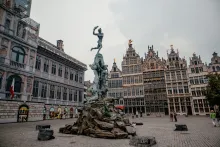 Panoramic view of Antwerp, Belgium featuring the historic old town, cathedral spire, riverside architecture along the Scheldt River, and colorful European rooftops under golden evening light.