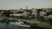 Panoramic view of Belgrade with the confluence of the Danube and Sava rivers, historic fortress walls, city skyline, and urban architecture at sunset in Serbia.