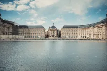Panoramic view of Bordeaux with elegant stone architecture, the Garonne River waterfront, historic city squares, and warm sunset light reflecting across the classical French skyline.