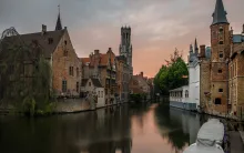 Panoramic view of Bruges with its medieval canals, historic brick buildings, Belfry tower, and calm waterways reflecting traditional Flemish architecture in Belgium at sunset.