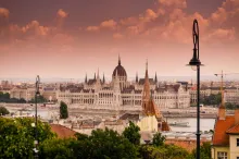 Panoramic view of Budapest with the Danube River, Hungarian Parliament building, historic bridges, and illuminated city skyline under warm evening light in Hungary.