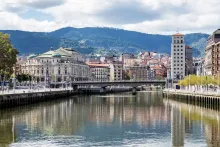 Panoramic view of Innsbruck, Austria featuring colorful alpine buildings, the Inn River, historic old town rooftops, and dramatic snow-capped mountains surrounding the city.