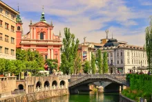 Panoramic view of Ljubljana, Slovenia, featuring the Ljubljanica River, historic old town architecture, Ljubljana Castle on the hill, and red-roofed buildings surrounded by green hills.