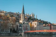 Panoramic view of Lyon, France featuring historic riverside architecture, colorful old town buildings, bridges across the Rhône and Saône rivers, and the Basilica of Notre-Dame de Fourvière overlooking the city.