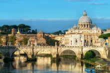 View of a historic bridge and cathedral in Rome with classical architecture, riverside scenery, and warm evening light in Italy.