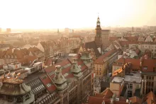 Panoramic view of Wroclaw, Poland featuring colorful market square buildings, historic church towers, cobblestone streets, and the Oder River winding through the city at sunset.