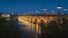 Panoramic view of Bordeaux, France, featuring elegant 18th-century architecture, the Garonne River waterfront, Place de la Bourse, and warm golden light over the historic city skyline.