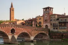 Panoramic view of Verona, Italy, featuring historic terracotta rooftops, medieval towers, the Adige River winding through the city, elegant bridges, and centuries-old Italian architecture beneath a clear blue sky.