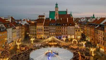 Panoramic view of Warsaw, Poland, featuring the colorful Old Town, historic church towers, royal architecture, modern skyline in the distance, and the Vistula River under a clear daytime sky.