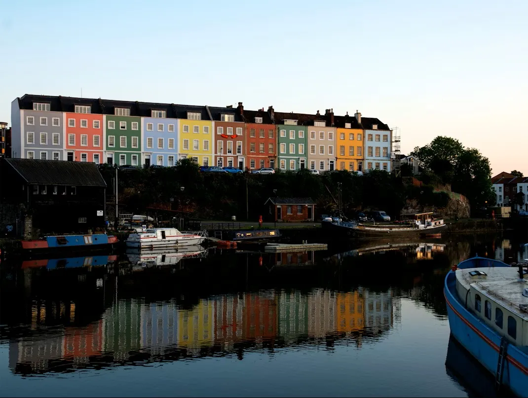 Row of vibrant, colorful houses in Bristol Harbour reflecting in the calm water at twilight, the perfect start for a Bristol to Liverpool road trip