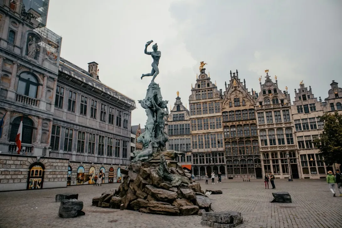 Panoramic view of the Antwerp skyline featuring the Cathedral of Our Lady and the MAS Museum reflecting in the Scheldt river at sunset