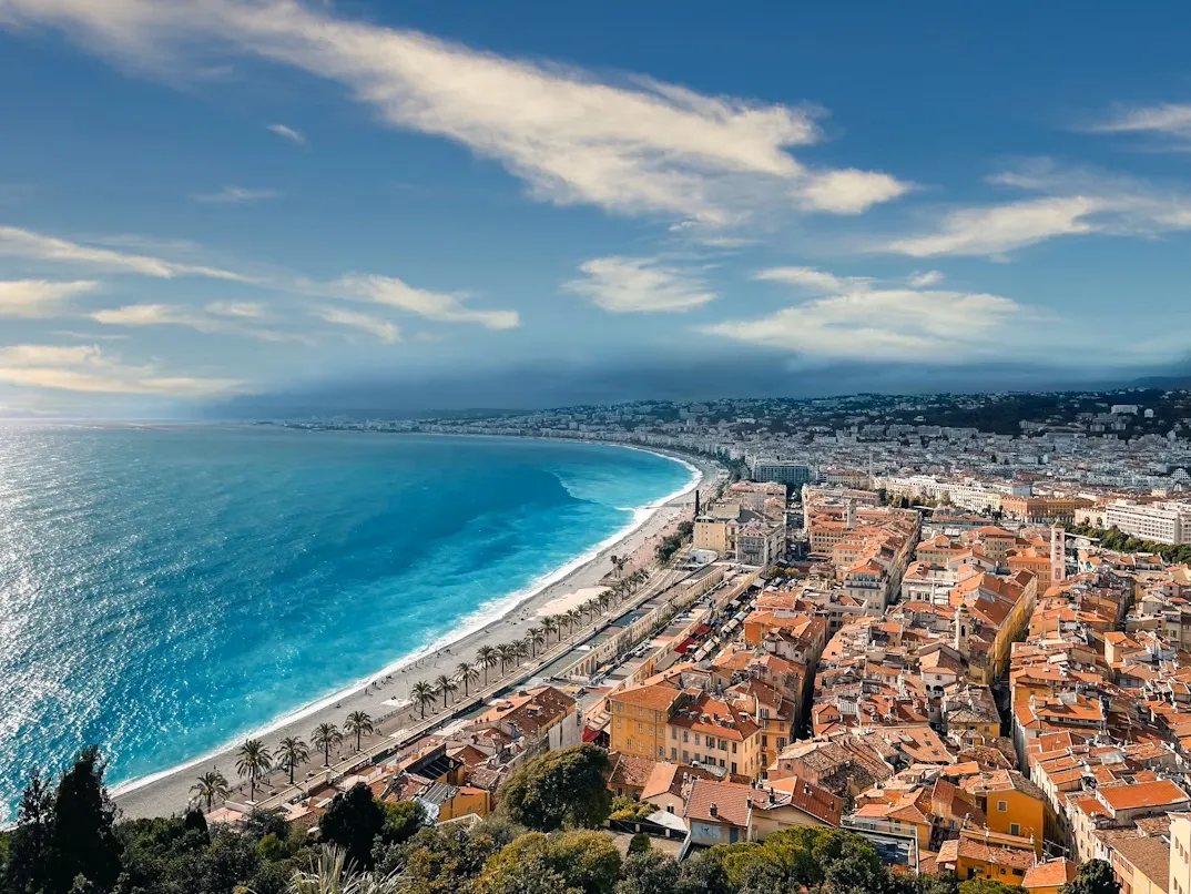 Panoramic view of Nice bay with Promenade des Anglais, blue Mediterranean sea, and terracotta rooftops of the old city.