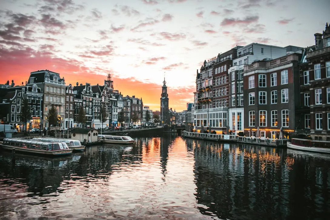 Panoramic view of Amsterdam canals with historic Dutch townhouses, bridges, bicycles, and waterfront architecture under warm evening light in the Netherlands.