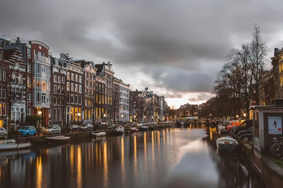 Panoramic view of Amsterdam with canal houses, bridges, bicycles, and historic Dutch architecture reflecting on the water under soft golden sunset light in the Netherlands.