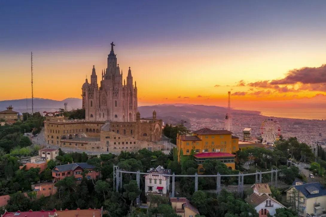 Panoramic view of Barcelona skyline with the Sagrada Família, Mediterranean coastline, and dense historic city architecture under golden evening light.