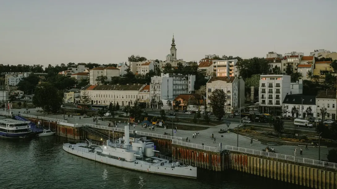 Panoramic view of Belgrade city skyline with the Danube River, historic Kalemegdan Fortress, and modern cityscape blending into the horizon at sunset.