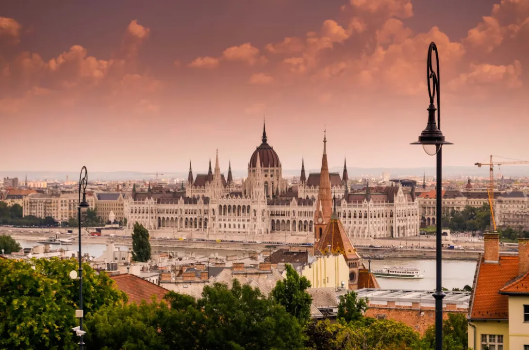 Panoramic view of Budapest with the Danube River, Hungarian Parliament building, historic bridges, and illuminated city skyline under warm evening light in Hungary.