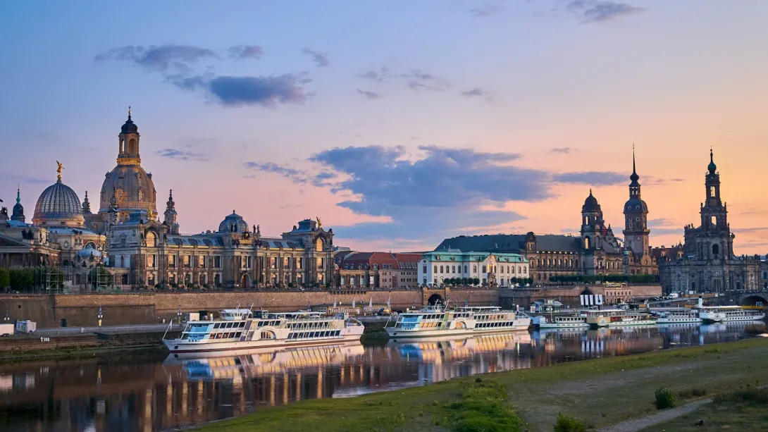 Panoramic view of Dresden skyline with historic baroque architecture, church domes, and the Elbe River at sunset in Germany.