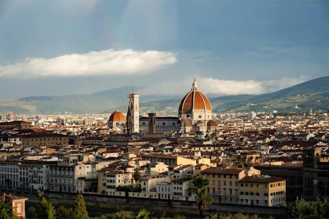 Panoramic view of Florence with the Duomo cathedral, terracotta rooftops, Arno River, and historic Renaissance architecture under golden evening light in Italy.