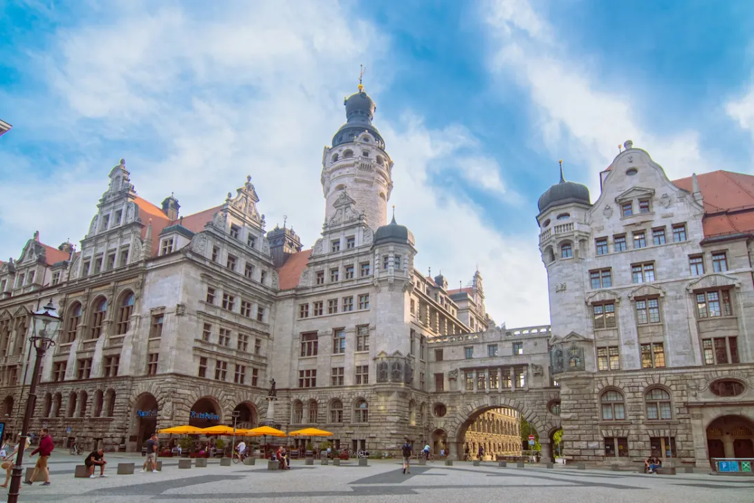 Panoramic view of Leipzig city skyline with historic buildings, church towers, and modern urban architecture blending into green parks under soft daylight.