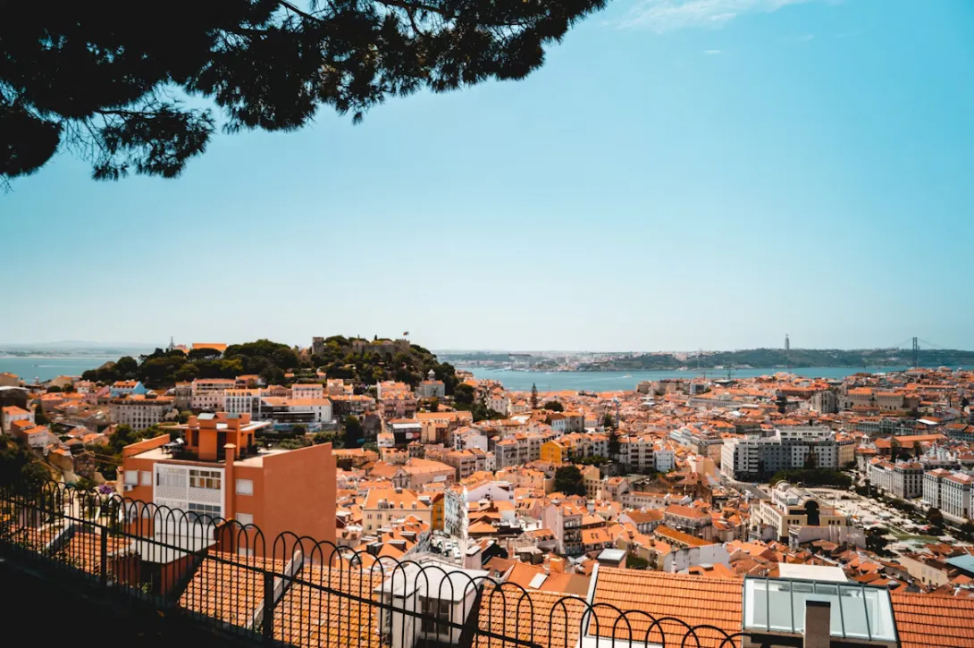 Panoramic view of Lisbon with colorful buildings, historic tram, and the Tagus River under golden sunset light in Portugal.