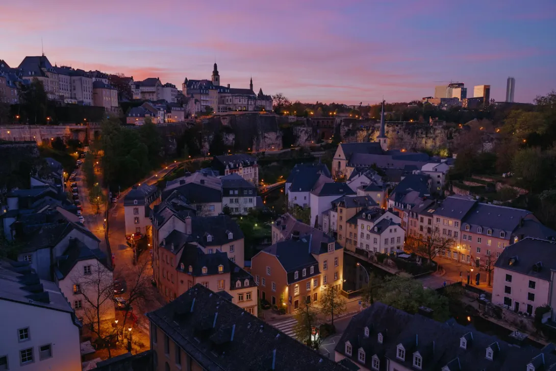 Panoramic view of Luxembourg City with historic fortifications, stone bridges, and colorful buildings surrounded by green valleys.