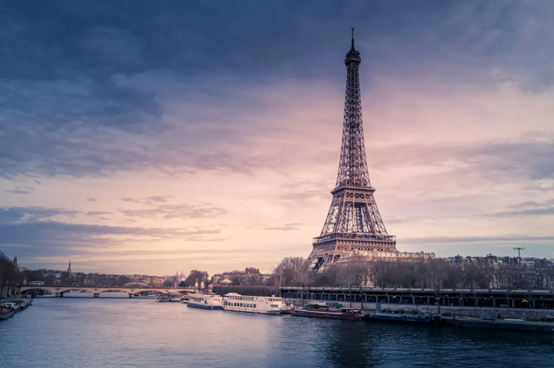 Panoramic view of Paris with the Eiffel Tower, Haussmann-style buildings, the Seine River, and classic French architecture glowing at sunset in France.