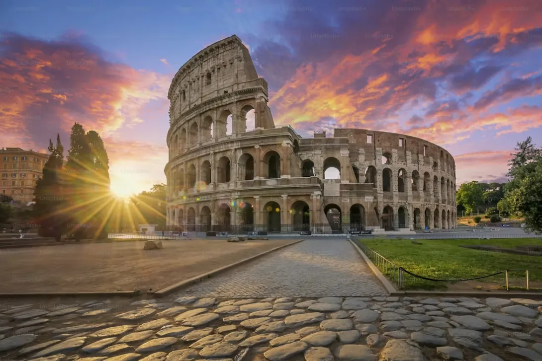 Panoramic view of Rome with the Colosseum, ancient ruins, historic rooftops, and warm Mediterranean sunset lighting over the Eternal City in Italy.