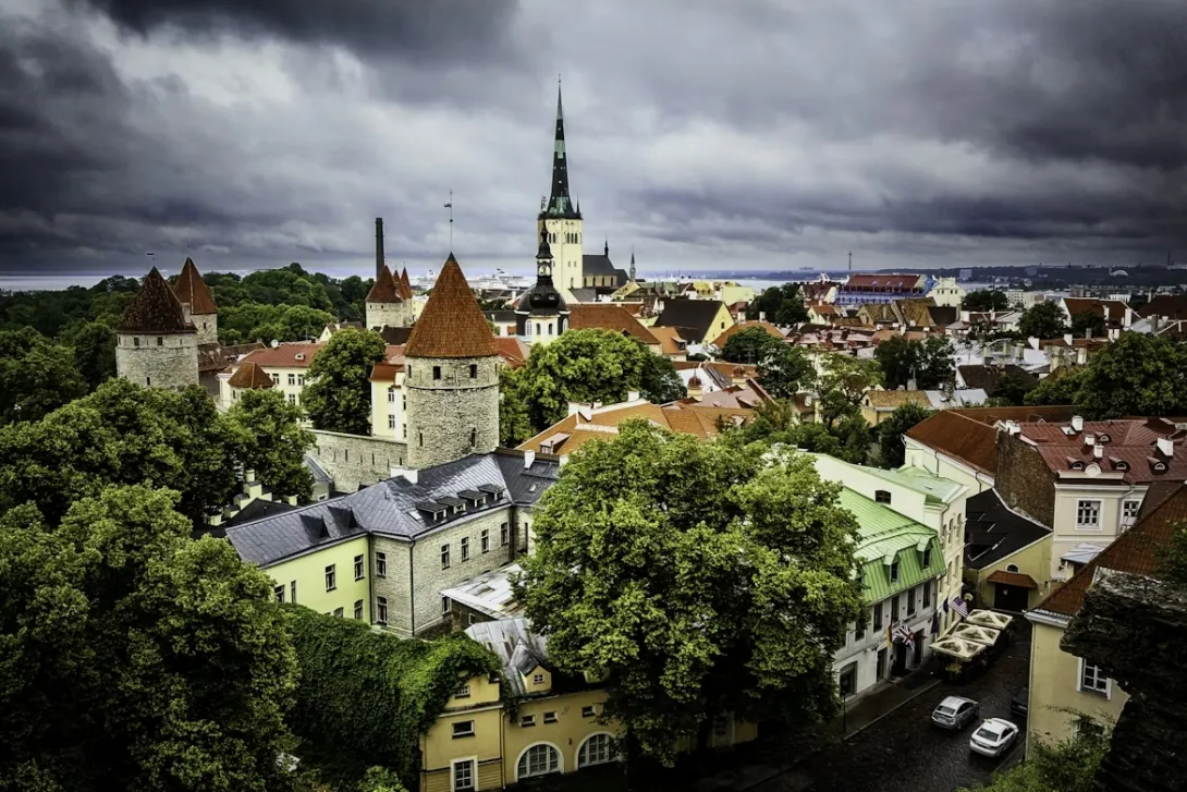Panoramic view of Tallinn, Estonia featuring the medieval Old Town skyline with red rooftops, church spires, and the Baltic Sea coastline under soft morning light.