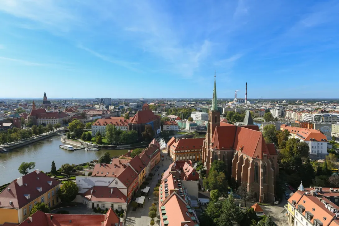 Panoramic view of Wroclaw market square with colorful historic townhouses, Gothic architecture, church towers, and lively old town streets under warm evening light in Poland.