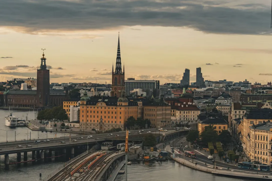 Panoramic view of Stockholm, Sweden, featuring colorful waterfront buildings, historic architecture, church spires, and islands connected by bridges under a bright Nordic sky.