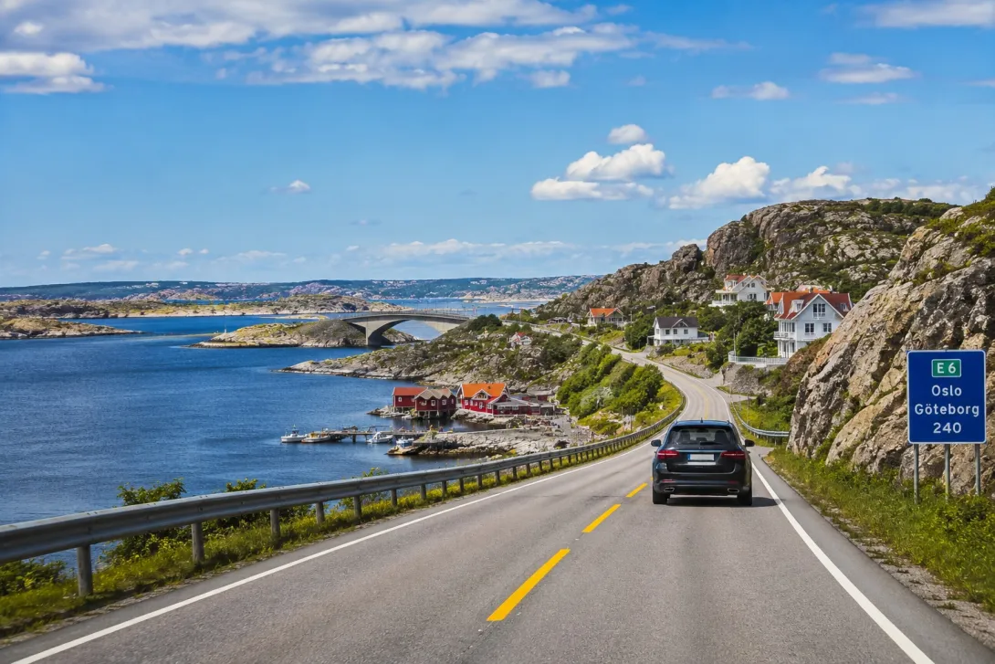 Car driving along the scenic coastal road from Oslo to Gothenburg with rocky shoreline, Nordic villages, bridges, and beautiful Scandinavian sea views.