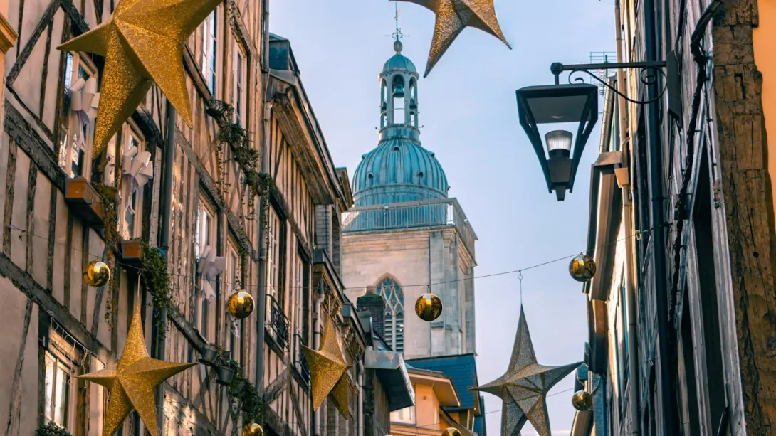 Panoramic view of Rouen, France, featuring the iconic Notre-Dame Cathedral with its Gothic façade, the Gros-Horloge astronomical clock, historic half-timbered buildings, cobblestone streets, and the charming skyline of Normandy’s capital under a soft blue sky.